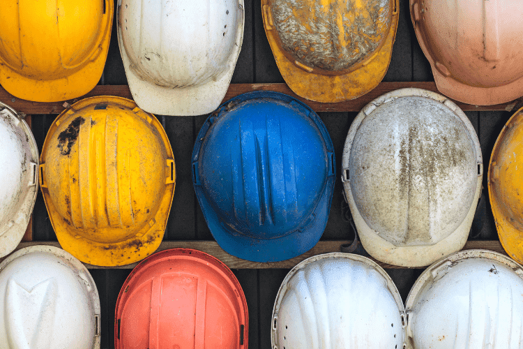 Collection of worn construction helmets in yellow, white, blue, and orange arranged on a wall.