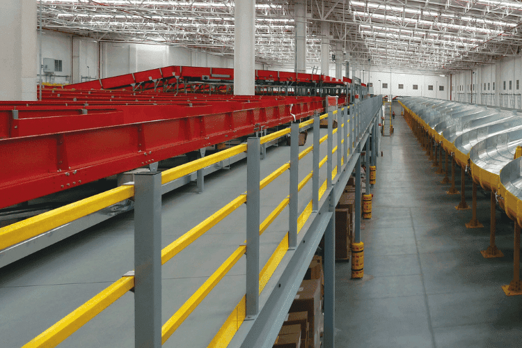 Automated warehouse with red conveyor systems and yellow safety railings along a mezzanine platform.
