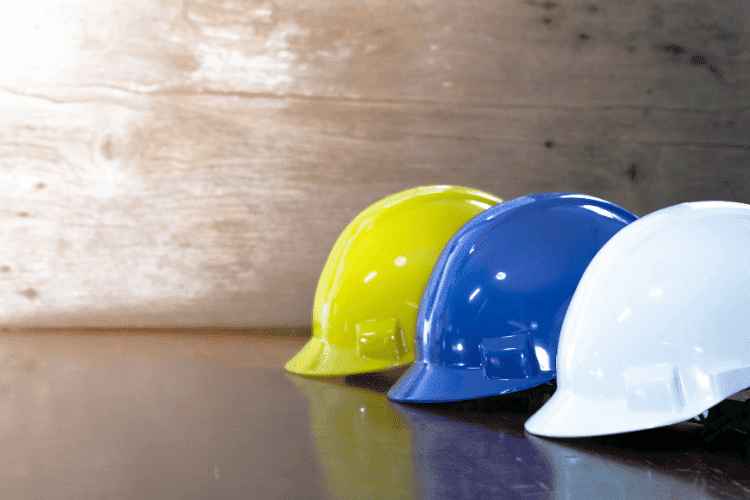 Yellow, blue, and white safety helmets arranged on a reflective surface against a wooden background.