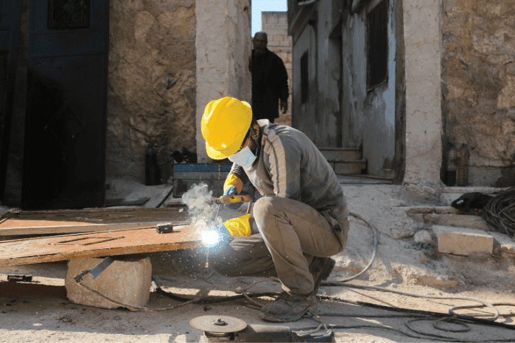 Worker wearing a white hard hat, protective mask, neon vest, and red gloves showing readiness for work.