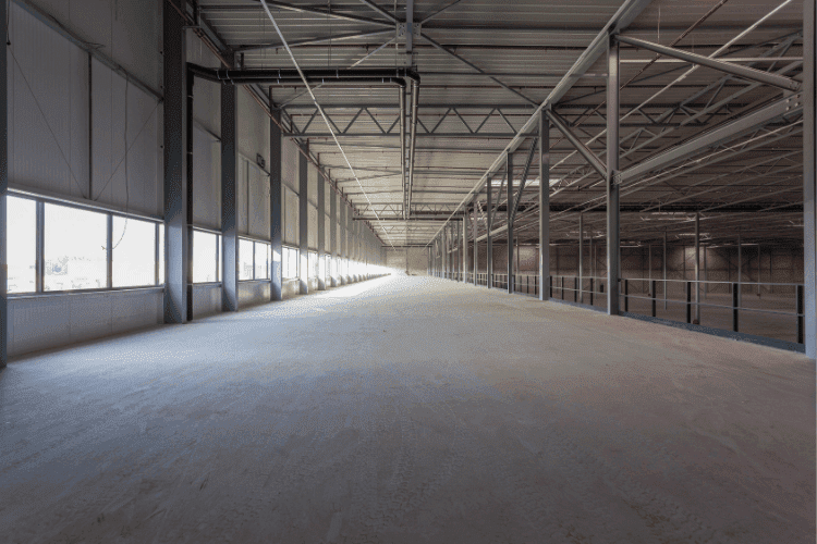 Wide, empty industrial mezzanine with concrete flooring and steel framing under natural light.