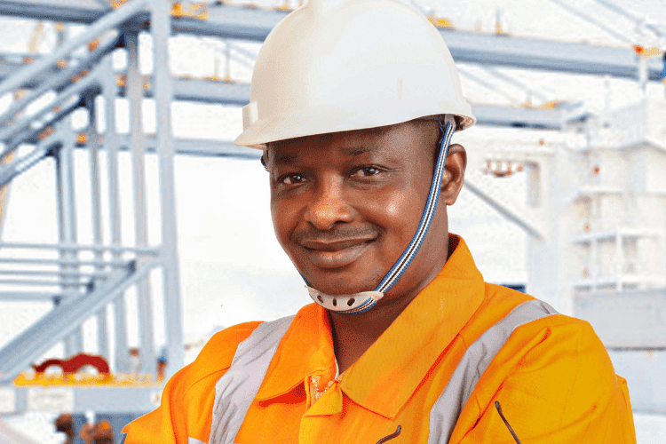 Industrial engineer wearing orange uniform and white hard hat standing confidently at a worksite.