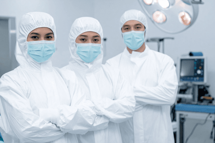 Medical professionals in full-body white protective suits and face masks standing confidently in a sterile environment.