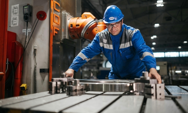 A factory worker wearing a hard hat, safety glasses, and protective coveralls operates heavy industrial machinery. The image highlights the importance of proper PPE in manufacturing environments to reduce risk and maintain safe working conditions.