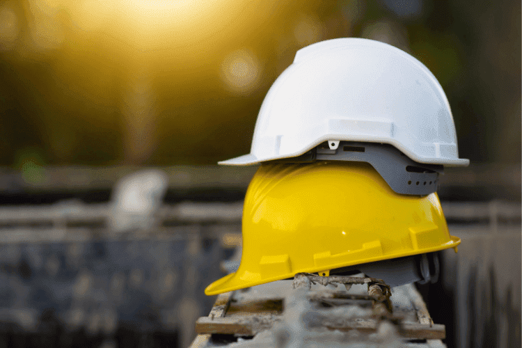 White and yellow construction helmets stacked on a beam at a worksite during sunset.