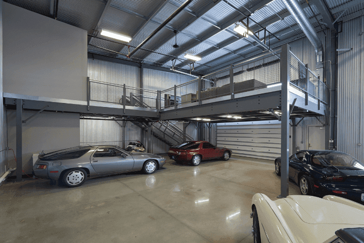 Spacious garage with steel mezzanine level and several parked sports cars below.