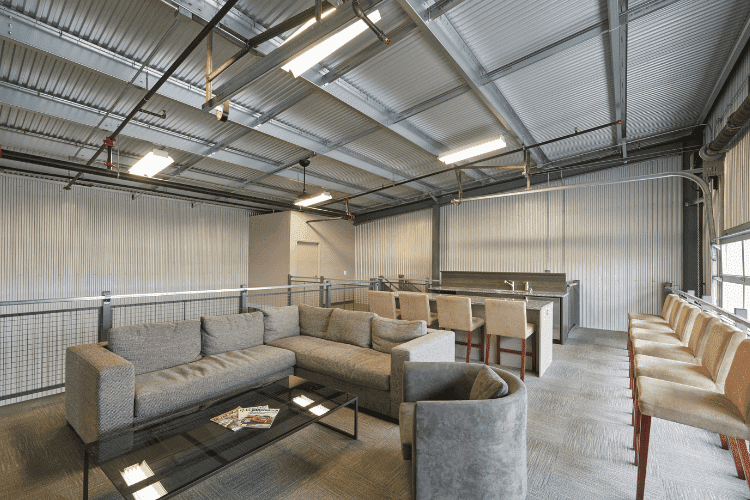 Modern warehouse mezzanine converted into a lounge area with sofas, bar stools, and overhead lighting.