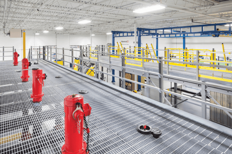 Steel mezzanine walkway with safety rails and red fire suppression valves inside a modern warehouse.